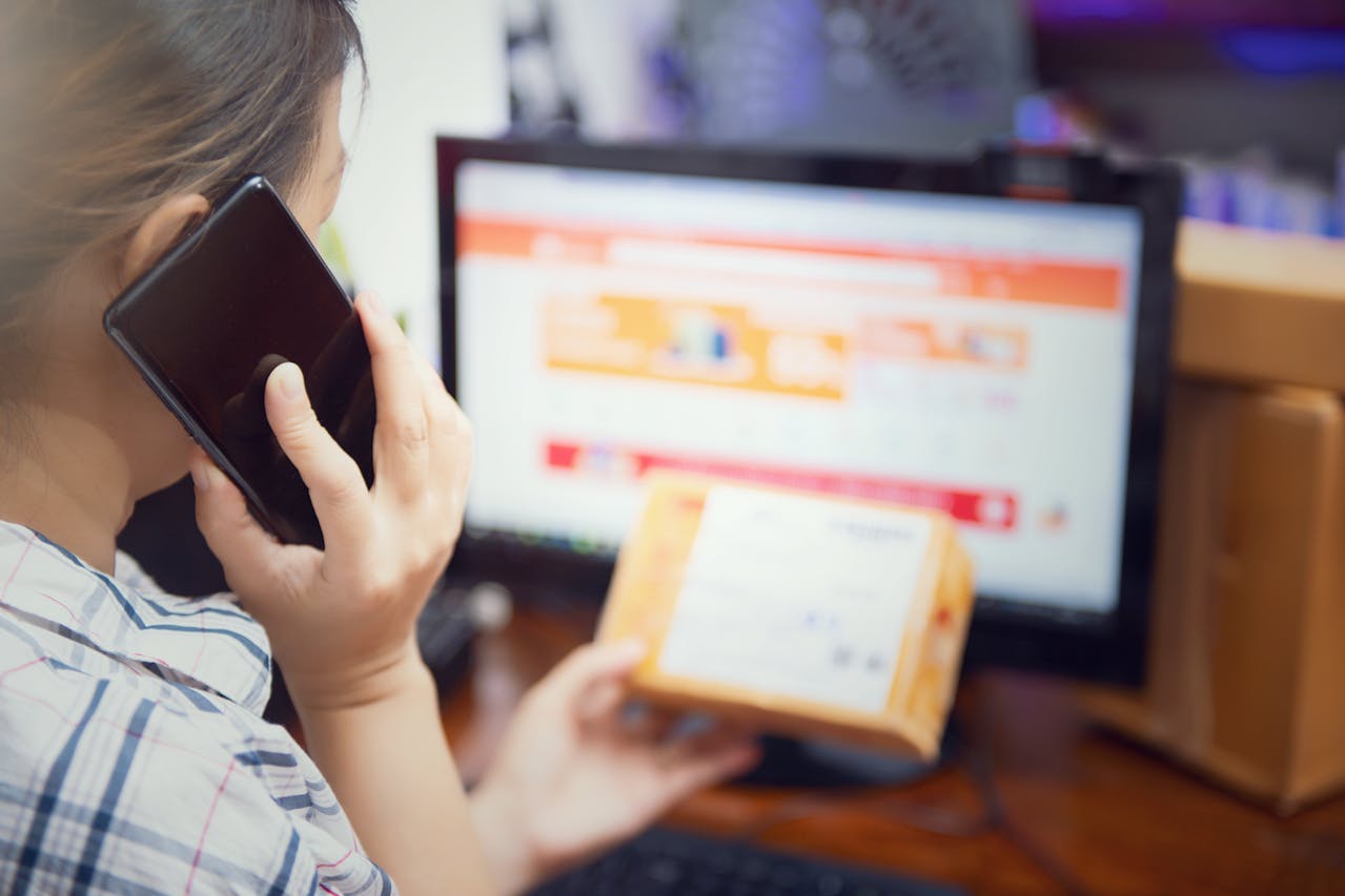 Osoba rozmawiająca przez telefon i trzymająca paczkę przy komputerze – ilustracja modelu sprzedaży dropshipping i współpracy z dostawcami.